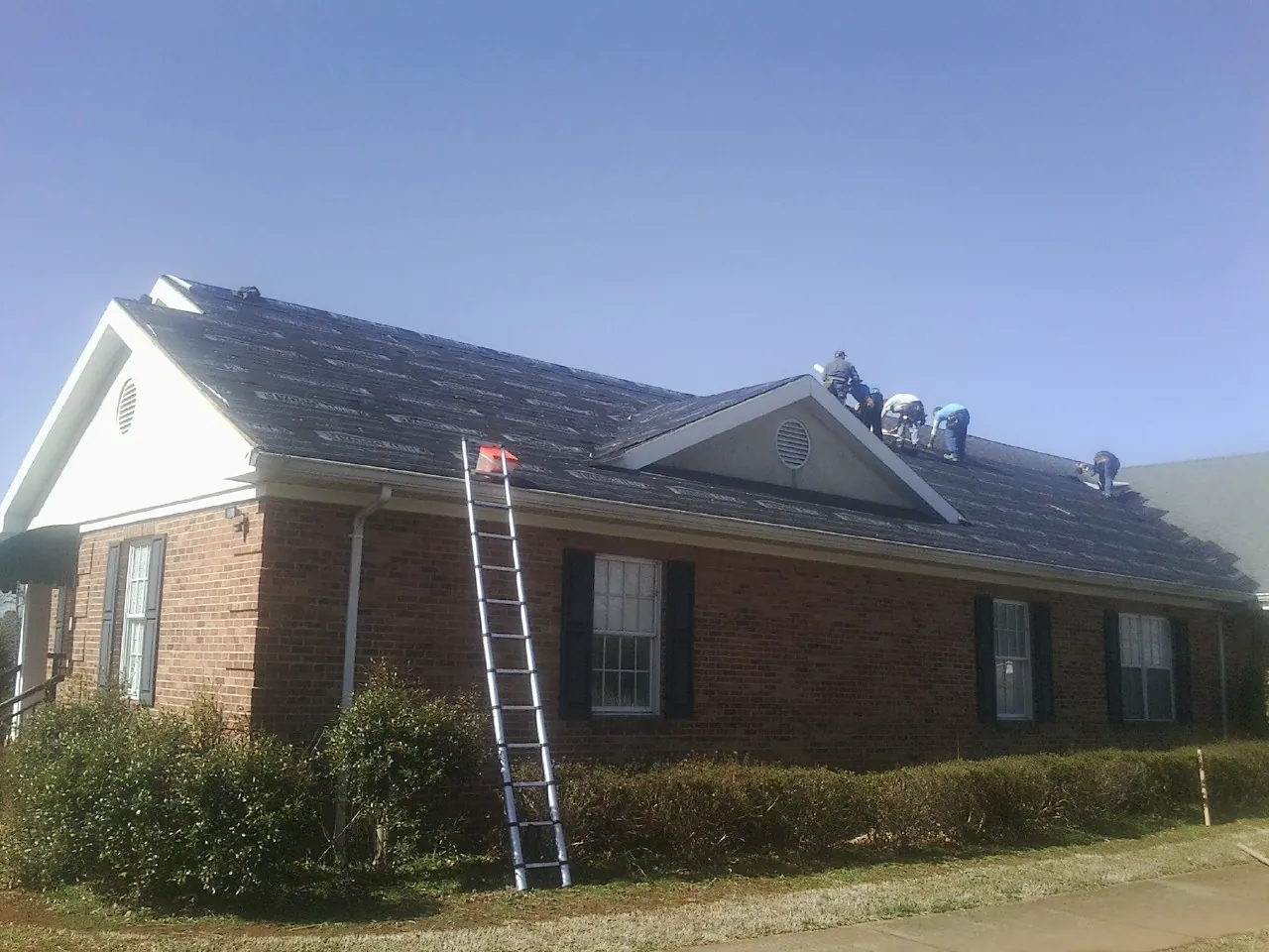 Crew tearing shingles off a brick ranch roof with a ladder set — Metal Roof Repair work by our crew in Bath